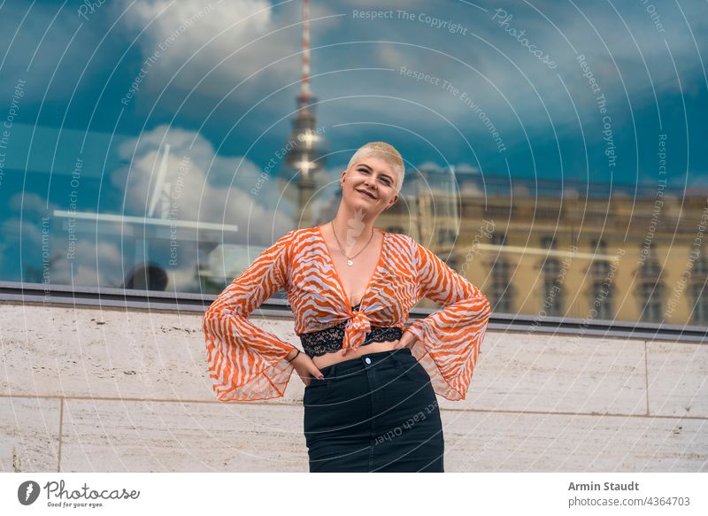 portrait of a young smiling woman with the berlin tv tower in the background studio confident outdoor window mirroring town city orange bustier blouse happy