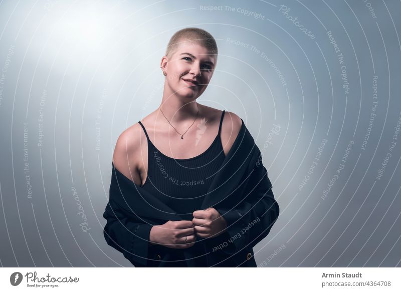 studio shot of a young, smiling woman with very short blonde hair in black clothes confident business smile shy timid lucky laugh piercing jewelry portrait