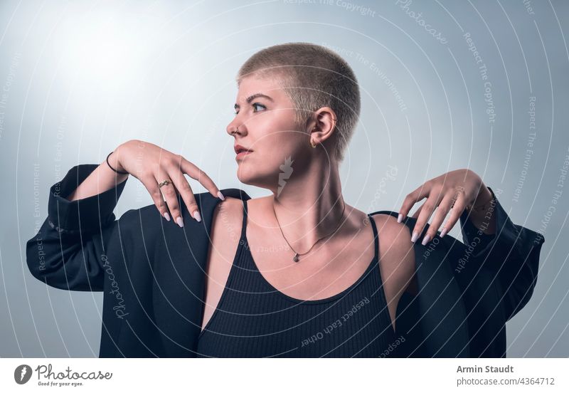 studio shot of a young, strong woman with very short blond hair in black clothes serious confident power powerful business piercing jewelry blonde portrait