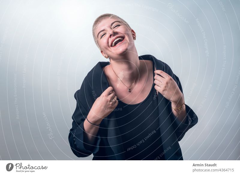 studio shot of a young, strong, laughing woman with very short blond hair confident passion business smile lucky piercing jewelry blonde portrait female