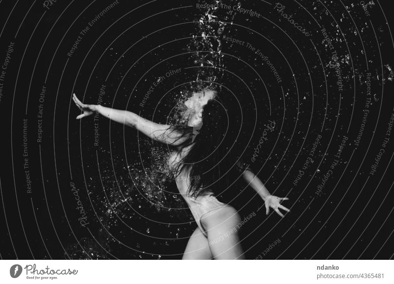 young beautiful woman of Caucasian appearance with long hair dances in drops of water on a black background. Jumping and swinging arms action active adult