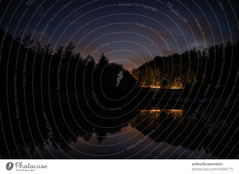 Night shot of calm water under starry sky with car lights in distance in forest Nature Exterior shot Deserted Landscape Lake Water stars Starry sky Starlit