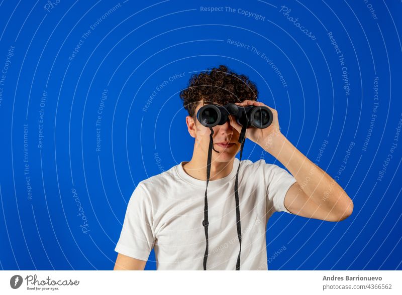 Young man over isolated blue background and looking in the distance with binoculars young hole humor model person photogenic portrait positive signs smile