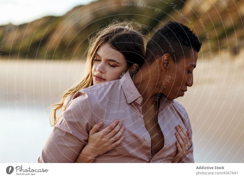 Tender multiethnic couple embracing on beach embrace love from behind seashore tender serene hug relationship multiracial diverse black african american