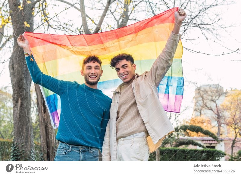 Happy gay couple with LGBT rainbow flag in park lgbt men pride equal homosexual tolerance male love together same sex lgbtq young freedom gender right smile