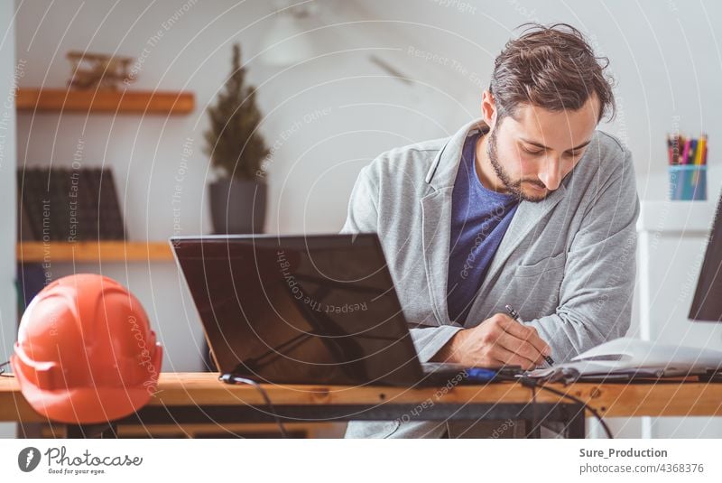 The designer thought and bowed his head while working with drawings and computers at the table on which the helmet lies. Color graded small business architect