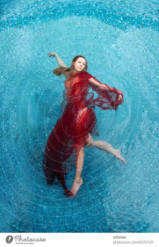 beautiful young woman relaxed in red dress, towel happily floating in the turquoise water in the pool, like walking in the air, copy space women weightlessly