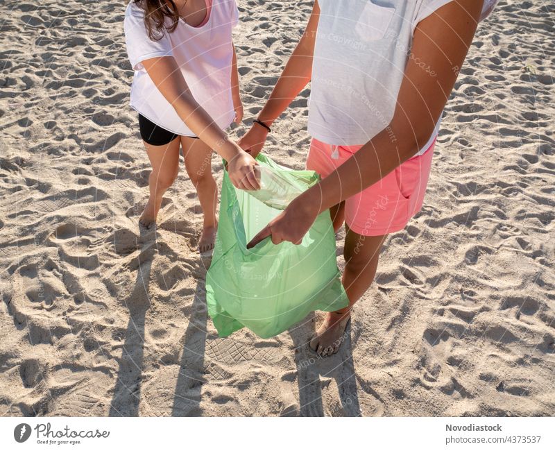 two girls collecting plastic on the beach, no faces shown environmental bag picking pecking people ecology male volunteer garbage rubbish rubber hand man human