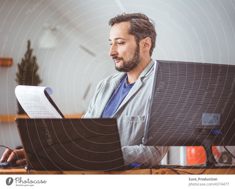 A man in the room is studying the documents. A man in casual clothes at a laptop. Work remotely business computer businessman casual clothing communication