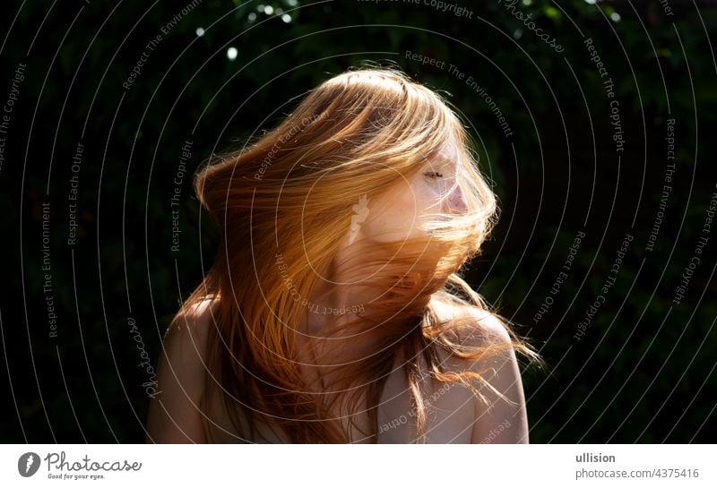 Sensual sexy portrait of young beautiful redheaded woman shakes her red hair outdoors in the sunlight with ivy background and green leaves, copy space amazing