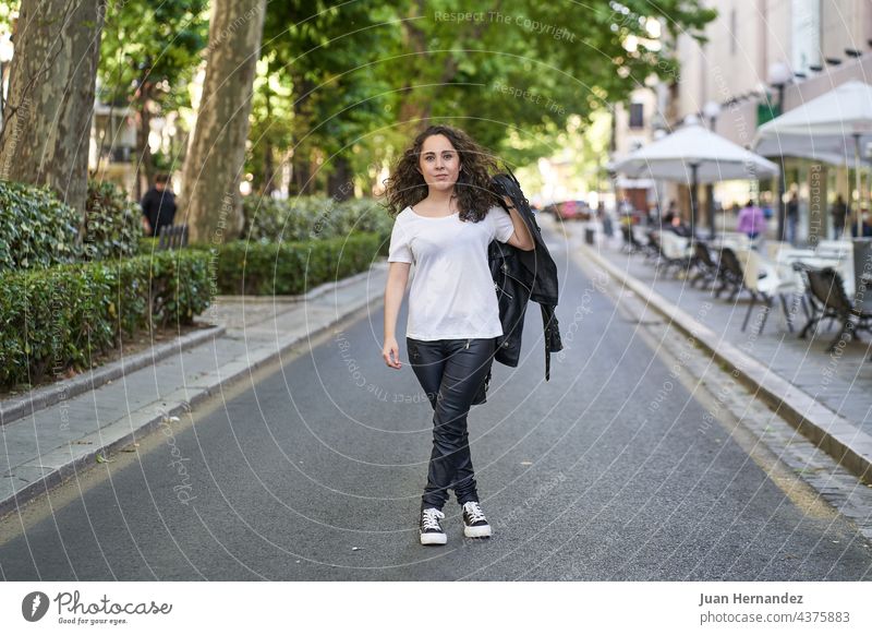 young woman dressed in black leather and white t-shirt in the middle of the road hispanic age 20s freedom happy happiness lady alone standing urban city street