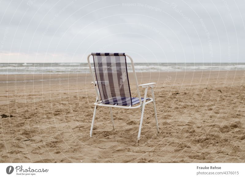 Blue and white folding chair on the beach at sunset - a Royalty