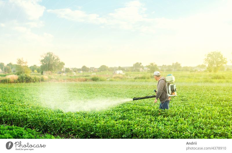 A farmer with a mist blower sprayer walks through the potato plantation. Use chemicals in agriculture. Agriculture and agribusiness. Treatment of the farm field against insect pests, fungal infections