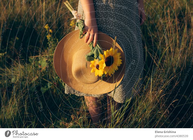 The girl holds a hat and a bouquet of sunflowers in her hands. summer grass field sunset slowdown silence closeness to nature natural seclusion self-discovery