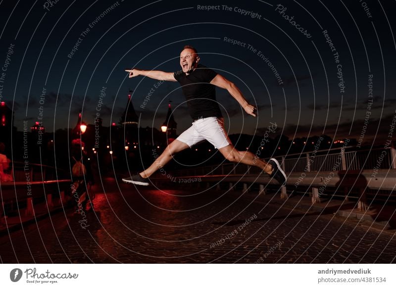 Adult young man in black t shirt and white shorts is jumping and having fun near the old castle in the evening. Fun concept, Kamyanets Podilskyy, Ukraine