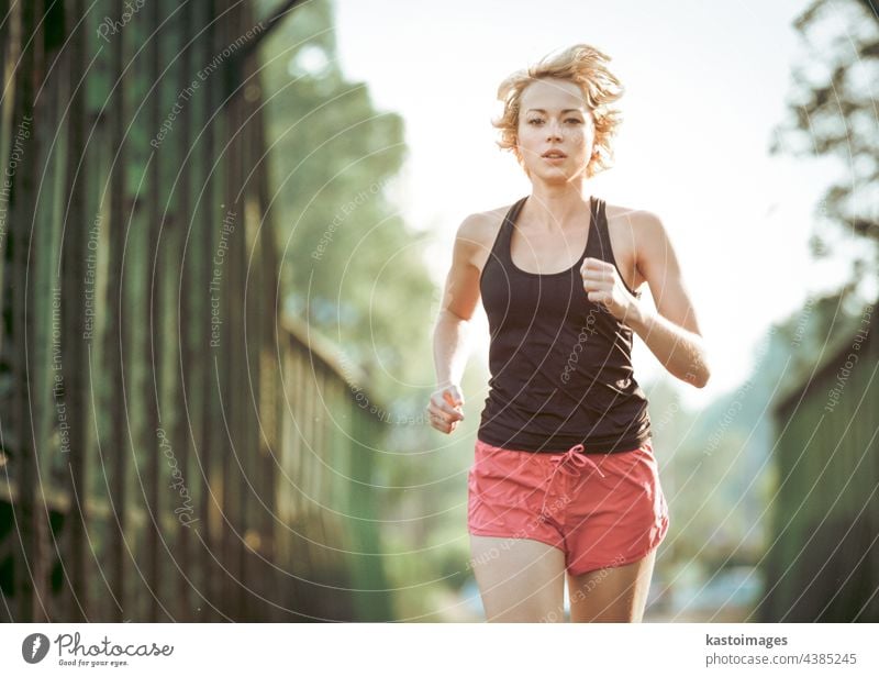 Athlete running on railaway bridge training for marathon and fitness. Healthy sporty caucasian woman exercising in urban environment before going to work. Active urban lifestyle