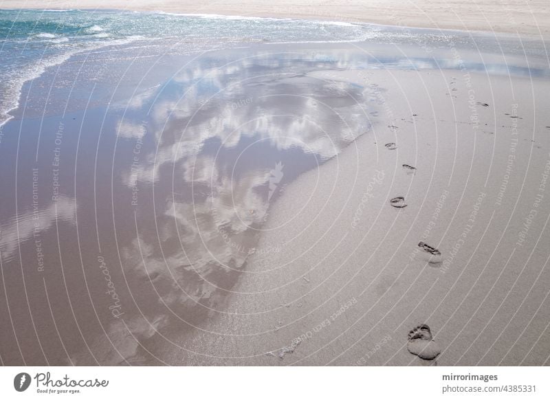 beach wet sand with fresh human bare footprints and blue cloud sky reflection and water waves seashore foot prints blue cloud sky reflection