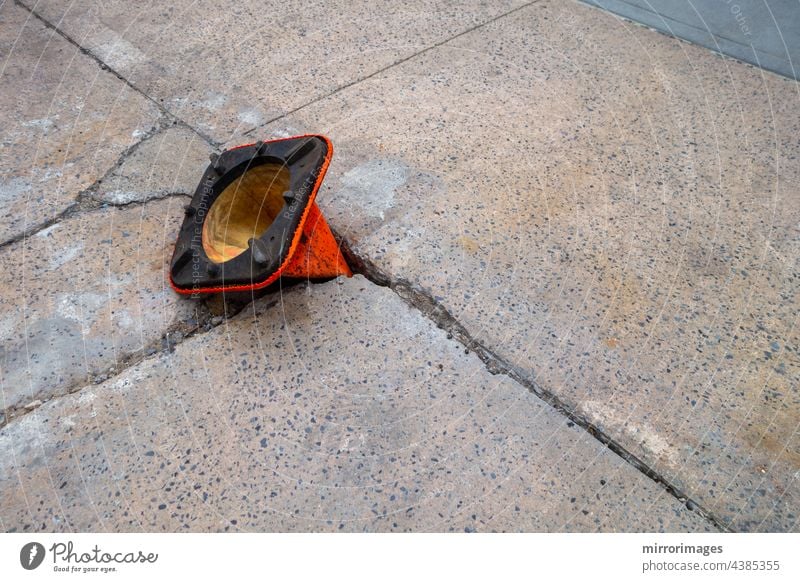 broken weathered sidewalk  with pot hole with orange cone upside-down in hole asphalt background black blue broken weathered street blacktop closeup concept