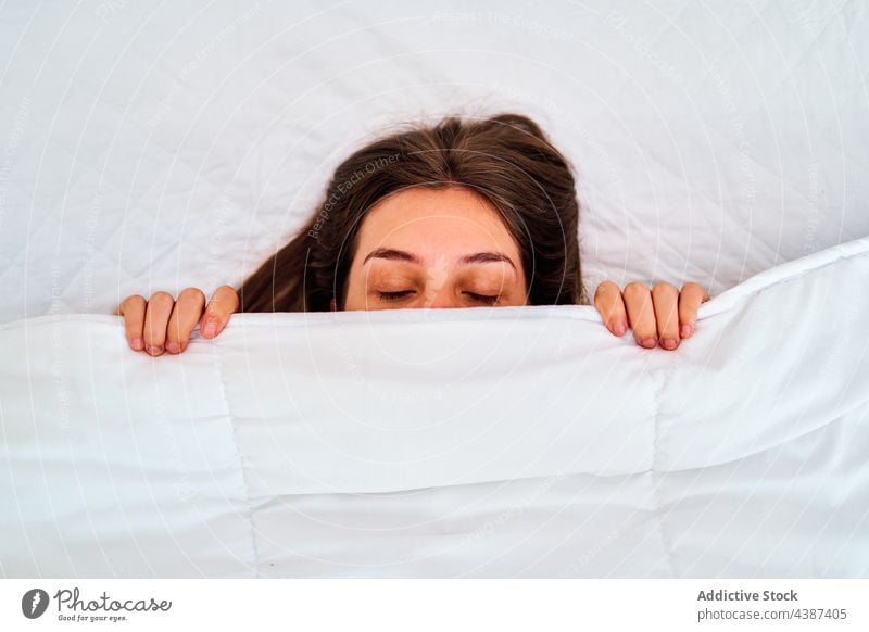 Young woman sleeping under blanket bed cover face cozy lazy morning rest home lying eyes closed relax comfort young peaceful soft white nap asleep tranquil