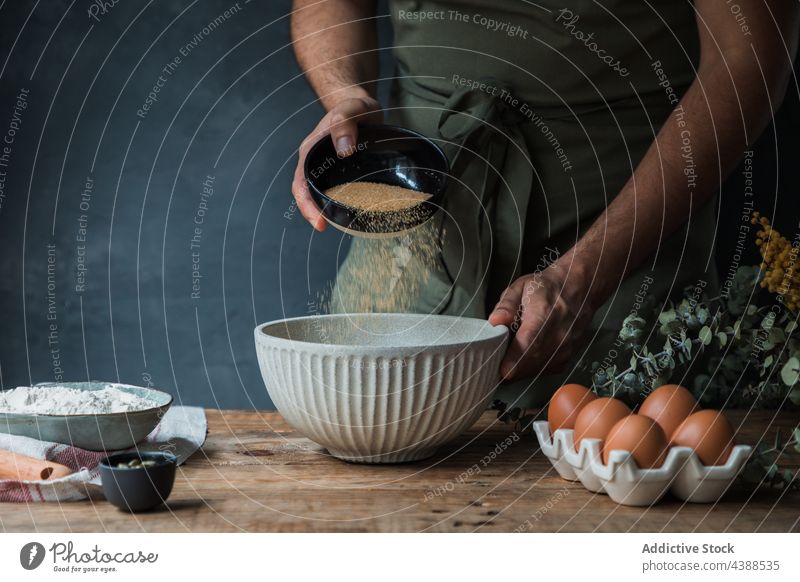 Crop cook adding cane sugar to pastry batter man bread bowl ingredient rustic table male apron egg flour food chef spill dessert cuisine culinary process