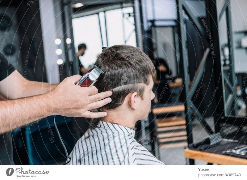 Barber makes a fashionable stylish haircut to a young man. Barbershop. Professional men's shaving and haircut, hair care. professional mens hairstyling