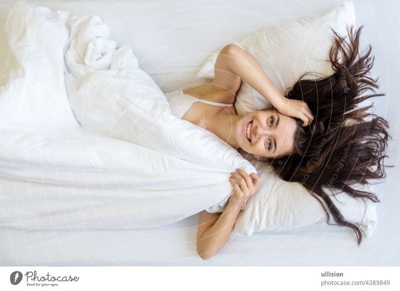 View from above to an attractive, young, sexy dark brown haired woman, smiling, laughing, enjoying the fresh soft bed, in the morning, copy space. smile