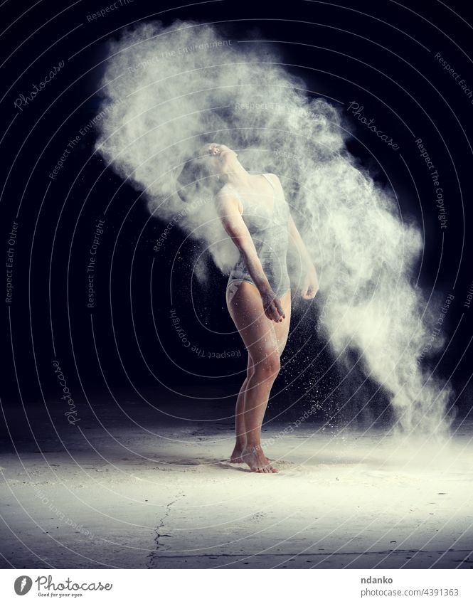 beautiful caucasian woman in a black bodysuit with a sports figure is dancing in a white cloud of flour on a black background action active adult art attractive