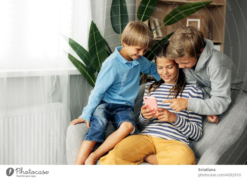 Children sit at home on the couch, play games on the phone, chat with friends. Modern technology and spending time at home tablet cute sister brother gadget boy