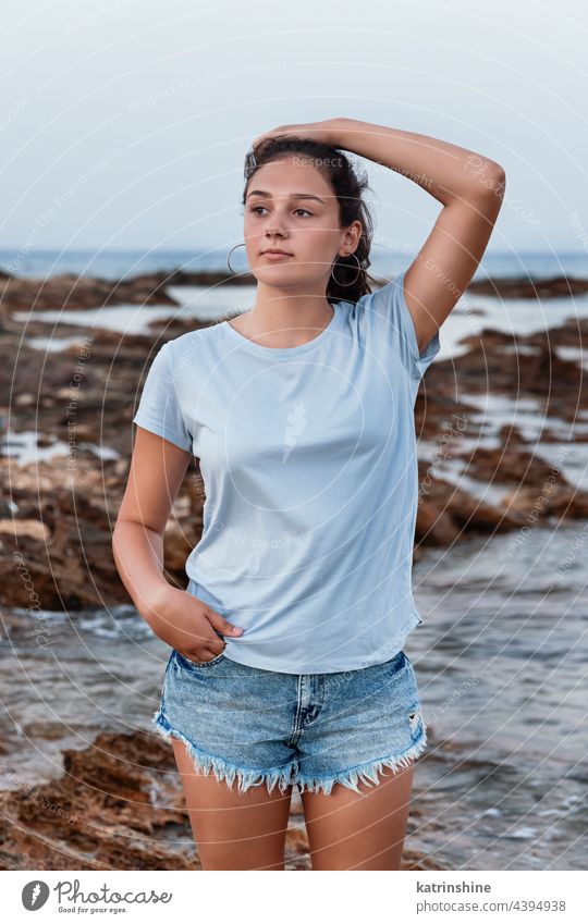 Teenage girl standing on cliff by the sea teenager mockup blue Caucasian rock sunset adolescent stone wearing t-shirts childhood female happiness copy space