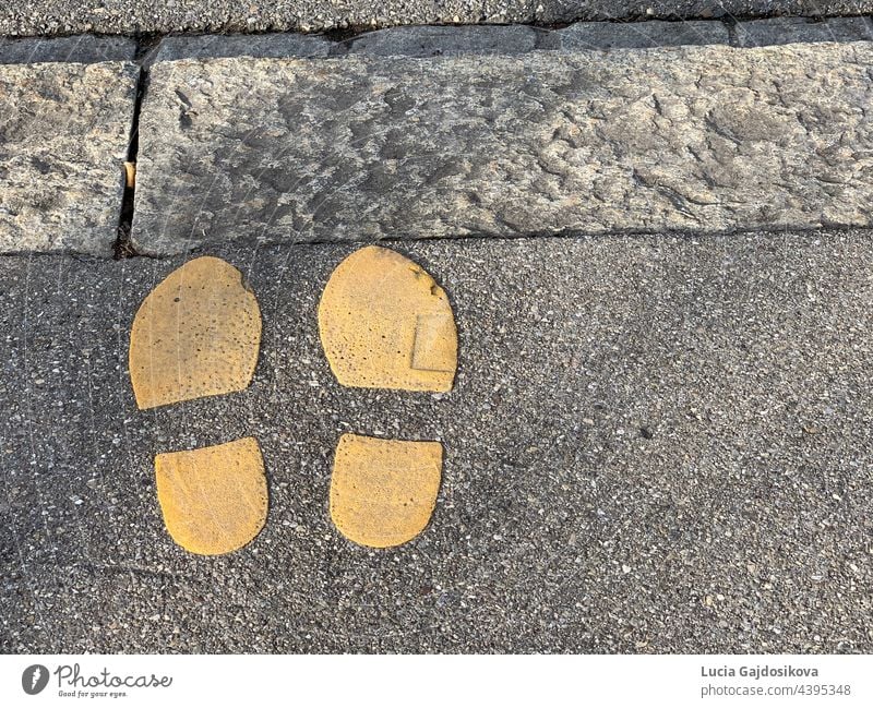 Two shoe imprints painted in yellow color on the edge of a sidewalk. Symbol for road crossing. There is copy space available. painted shoe imprints symbol