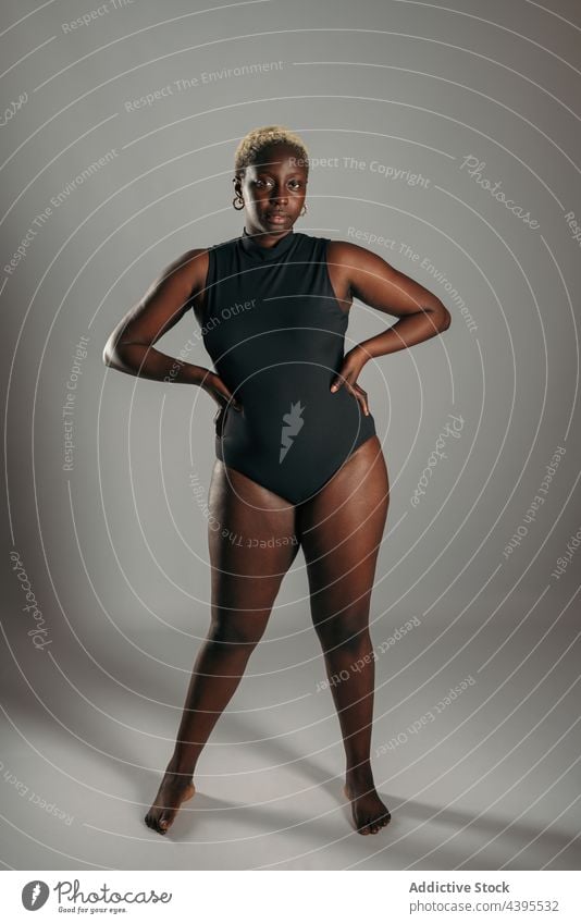 Serious woman with her hands on her hips in bodysuit in studio body positive curve shape delight female ethnic african american black optimist glad content