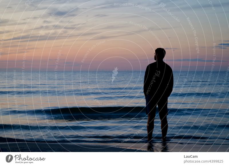 The sun has just set. In the evening atmosphere, a man stands on the beach in the water and looks into the distance.... Sunset Beach Twilight Twilight sky Ocean