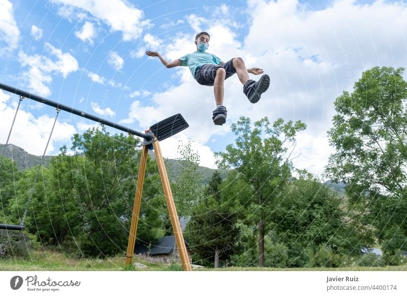 young guy wearing a sanitary mask makes a huge jump from a swing on a playground, leaping into the empty jumping flying face mask childhood outdoors boy fun