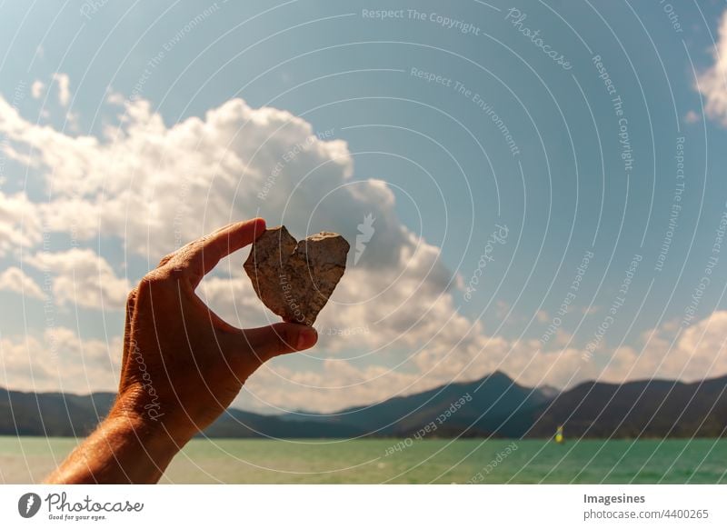 Hand holding a heart. Stone heart in a female hand on the background of the sky and the lake. Love for nature. Pre-Alps mountains and Walchensee in Bavaria, Germany