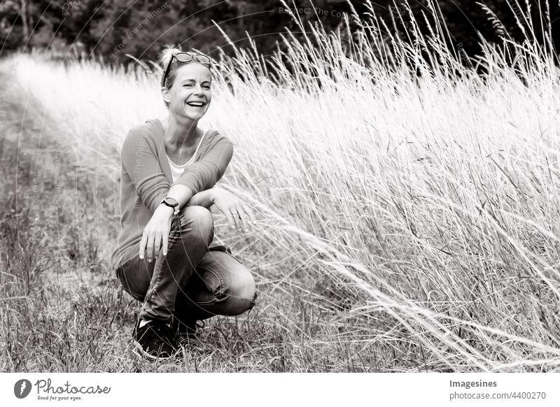 Black and white portrait of smiling happy and charming woman looking at camera. Portrait of woman in summer squatting on a meadow. black-white smilingly