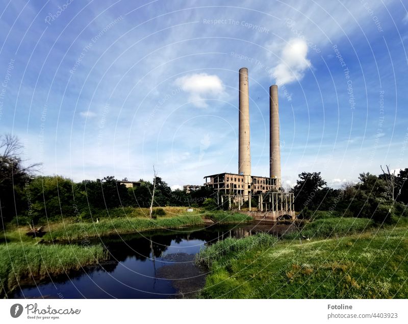 Lost Place - an old power plant on the Oder River that was built but never put into operation. 2 chimneys rise into the blue, slightly cloudy sky. lost place