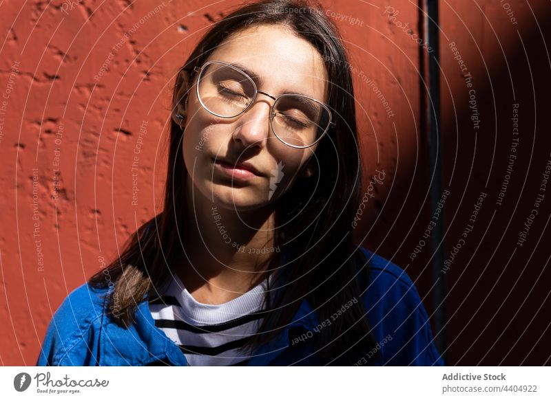 Dreamy woman enjoying sunny weather in city dreamy sunlight carefree eyes closed street tranquil shadow content female urban charming peaceful harmony wall