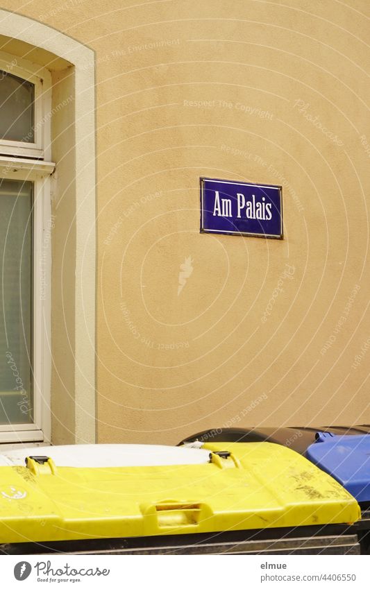 purple street name sign - Am Palais - on a beige house wall and two garbage containers in front of the window / living At the palace Street sign street sign