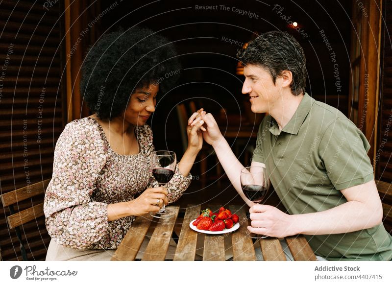 Content multiethnic couple with glasses during romantic date red wine cheers holding hands love multiracial diverse black african american relationship cheerful