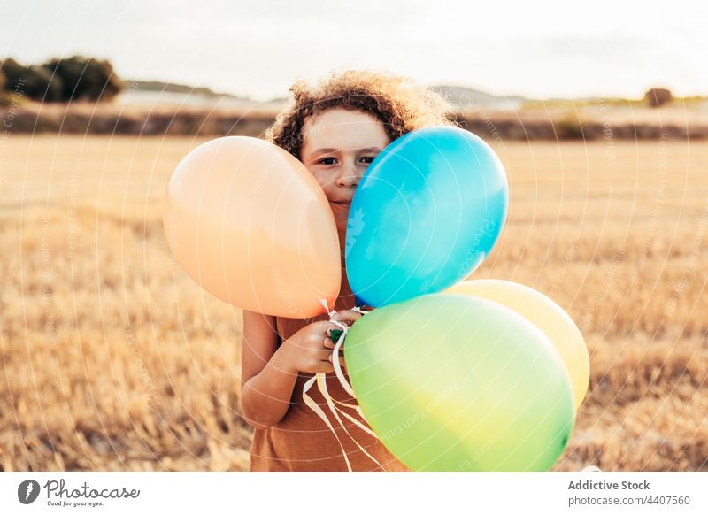 Carefree ethnic child playing with colorful balloons in field air balloon wind playful carefree freedom summer kid smile cheerful childhood happy cute fly