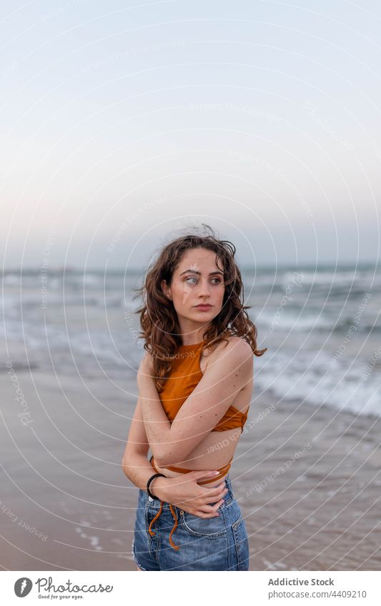 Young woman standing near sea beach wave evening dreamy coast seaside summer weekend female rest young water shore ocean relax long hair wavy hair feminine slim