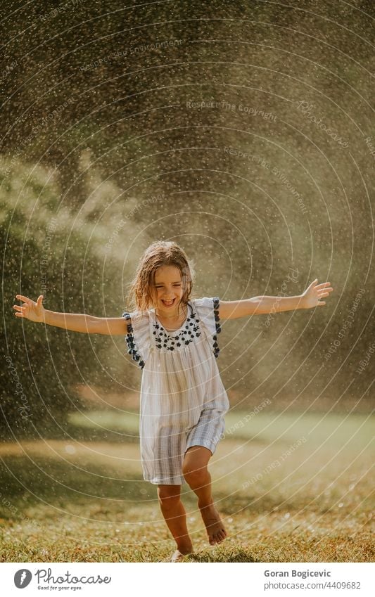 Cute little girl having fun under irrigation sprinkler happy kid summer happiness joy spray wet active water outdoor splash child activity young freedom leisure