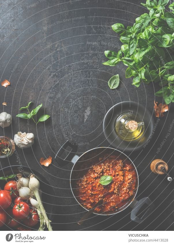 Delicious sauce Bolognese , made at home in a black pan with spoon and basil leaves on  dark kitchen table with fresh ingredients and olive oil. View from above. Frame. Food background