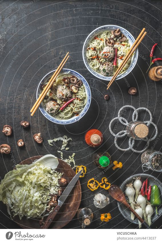 Asian food. Bowls with noodles and Shiitake mushrooms, chili pepper , chopsticks and meatballs on dark rustic background with fresh Asian cuisine ingredients and sauce jars. Top view