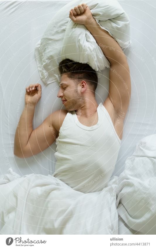 Bedtime. Top view of muscular young man in shirt stretches in bed in the morning, Copy space awake white comfortable fashion seducer sport valentine lover