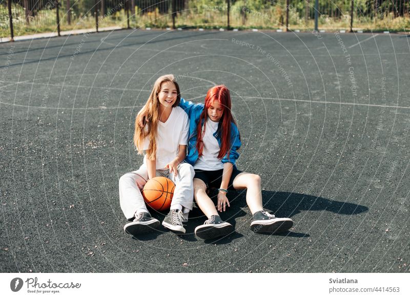 A couple of teenage girls on a sports street court with a basketball lifestyle relax after a game and talk. The concept of sports and a healthy lifestyle