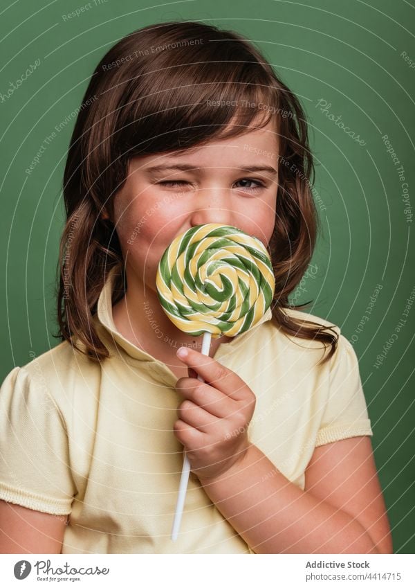 Cheerful girl with spiral candy on green background lick lollipop swirl sweet funny tongue out child kid dessert cute adorable happy tasty delicious stick treat