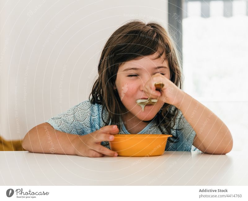 Funny girl eating cream soup during lunch child kid home delicious puree bowl table food meal childhood healthy nutrition cute yummy dish tasty spoon kitchen