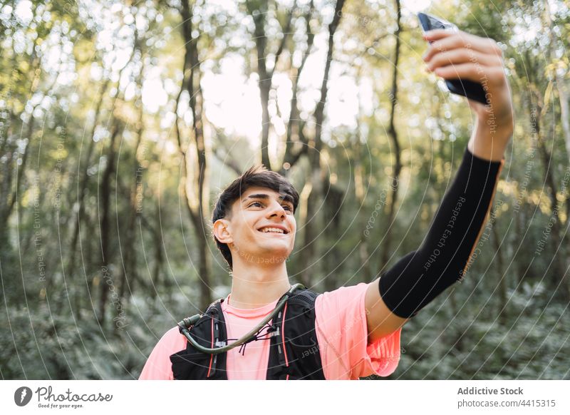 Smiling traveling man taking selfie with smartphone during hike traveler browsing backpack trekking forest using hiker male nature gadget smile content device
