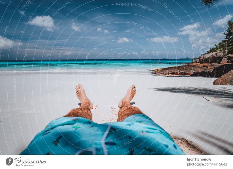 POV of male wearing swimming shorts with tanned legs on paradise white sand tropical exotic beach with view to turquoise blue ocean. Travel holidays vacation concept